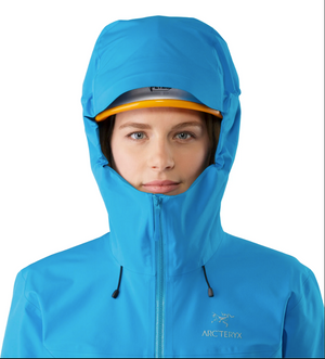 Person wearing a blue Arc'teryx jacket with a hood on a white background