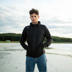 Devold Men's Nibba Merino Wool Jacket with Hood Full Zip in Black Lifestyle Photo on a Male Mode Standing on a Coastline | ScoutTech Outfitters