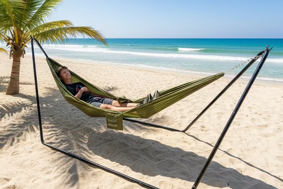 Young man laying in a green hammock for 1 Person by Europe Bound set up on a stand on a tropical beach