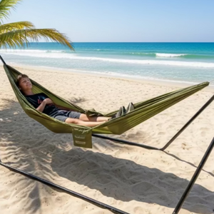 Young man laying in a green hammock for 1 Person by Europe Bound set up on a stand on a tropical beach | ScoutTech Outfitters