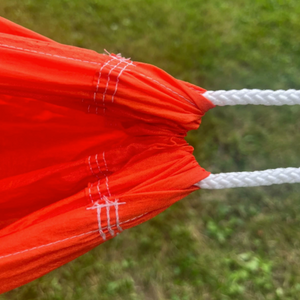 Close-up of a bright orange Europe Bound hammock with white braided ropes and white stitching, photographed outdoors against a blurred green grassy background. | ScoutTech Outfitters