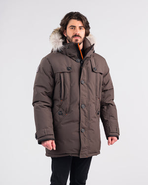 Man wearing a brown winter coat with fur hood on a white background